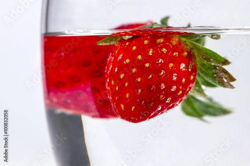 Close-up of water glass with several floating strawberries