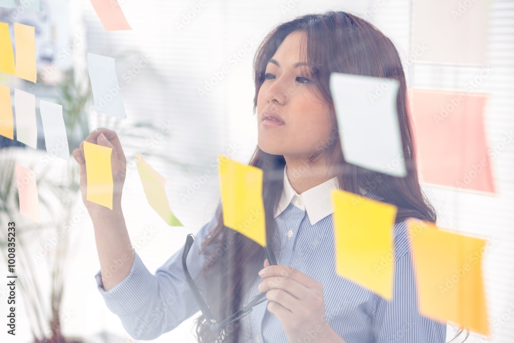 Asian businesswoman using sticky notes on wall Asian businesswoman using sticky notes on wall