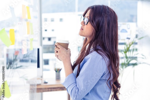 Businesswoman holding disposable cup and looking at wall 