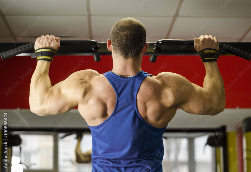 Naklejka premium Professional bodybuilder with ideal muscular body doing pull-ups in the gym 