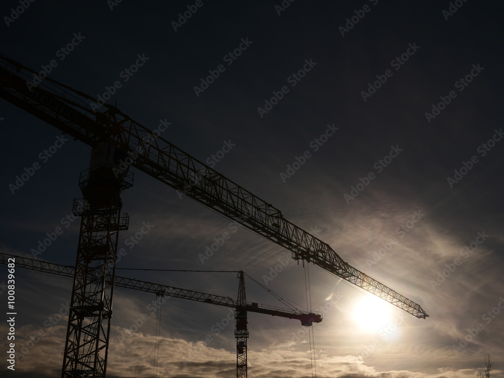Industrial construction cranes over sun at sunrise