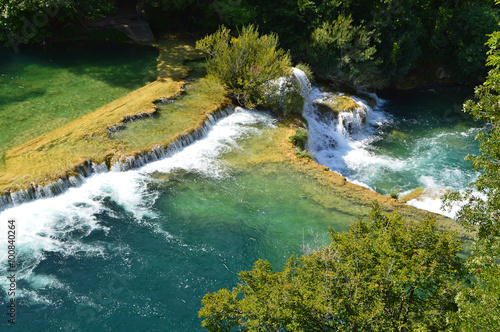 Green river and waterfall cascade surrounded by green trees