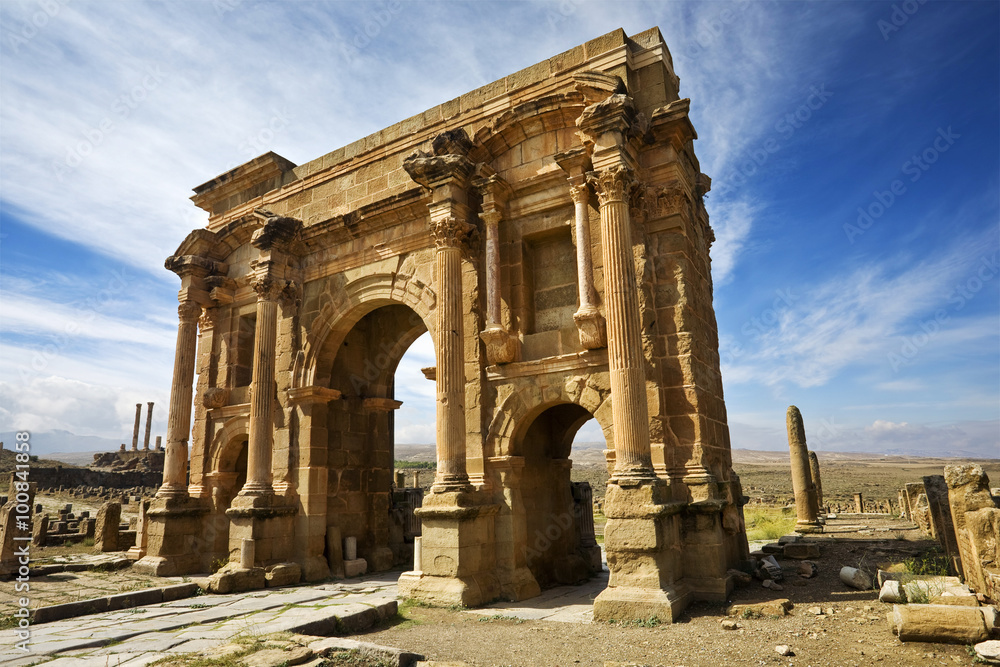 Naklejka premium Algeria. Timgad (ancient Thamugadi or Thamugas). Triumphal arch, called Trajan's Arch and fragment of Decumanus Maximus street