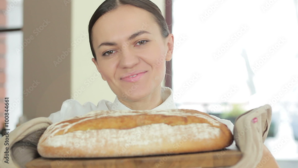 A young smiling woman standing in her kitchen holding freshly baked bread, close up A young smiling woman standing in her kitchen holding freshly baked bread, close up