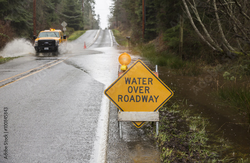 Emergency vehicle driving on flooded road with warning sign