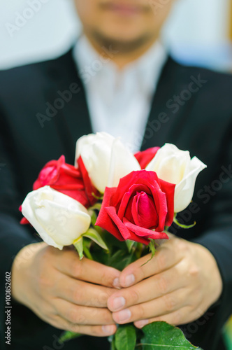 A man is giving white and red rose bouquet. Photo is focused at the middle red rose.
