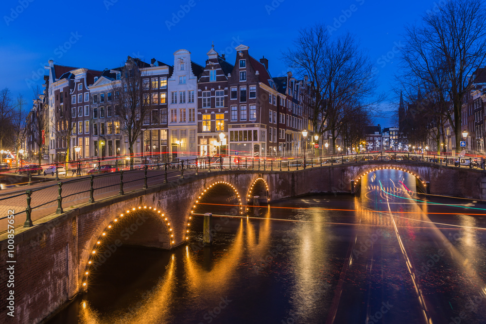 Night view over Amsterdam canals and bridges, with lights and their trails