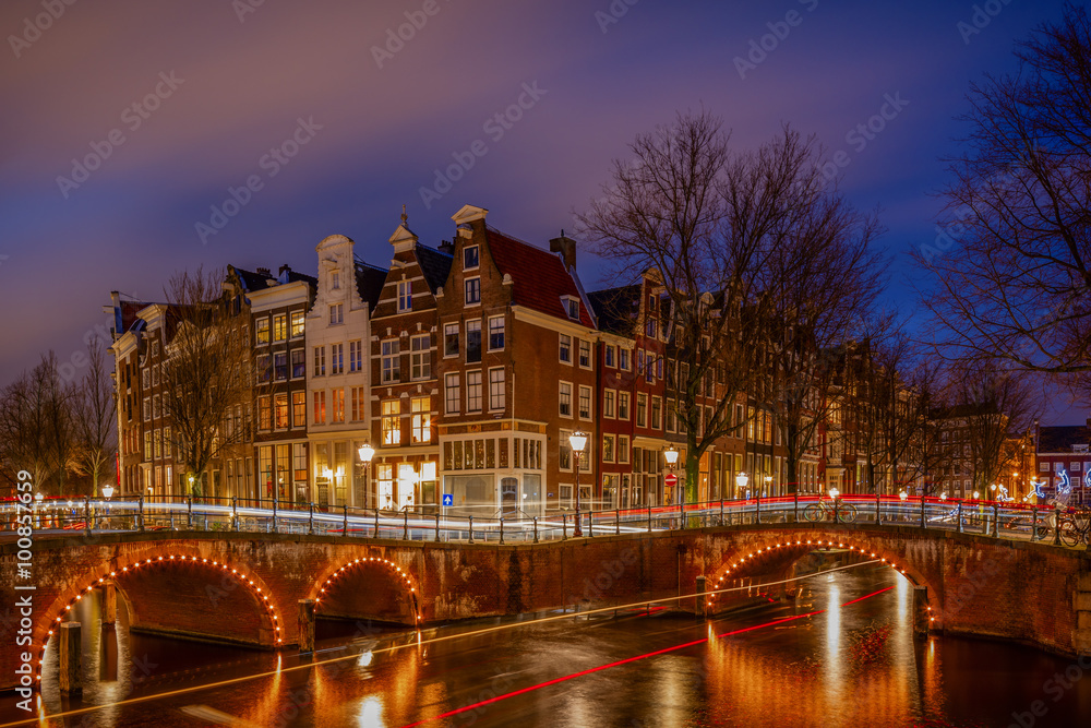 Night view over Amsterdam canals and bridges, with lights and their trails