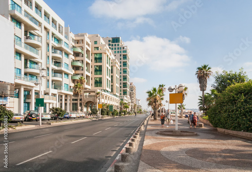 Highway along embankment with buildings on road side, parking and people walking along. Tel Aviv, Israel.
