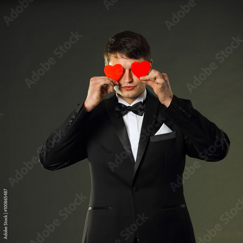nice handsome man in a tuxedo with a red paper hearts. On a black background.