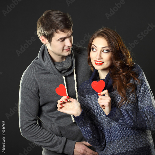 Ordinary beautiful couple having fun with a paper hearts on Valentine's Day. On a black background.