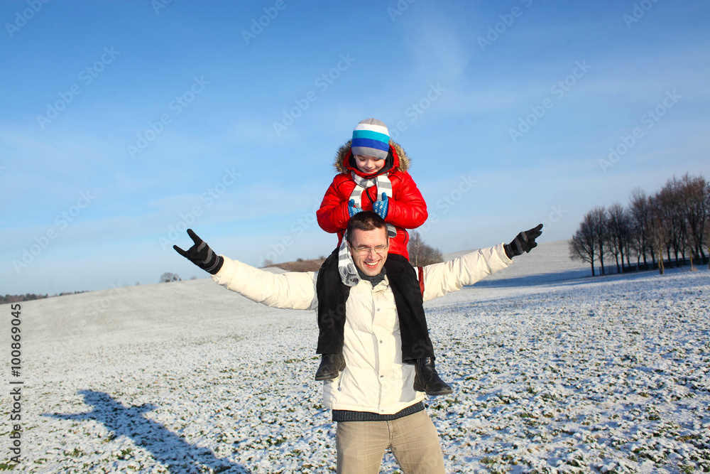 happy young father and his little son spending time outdoor in winter park. Son sits on his father's shoulders and having fun