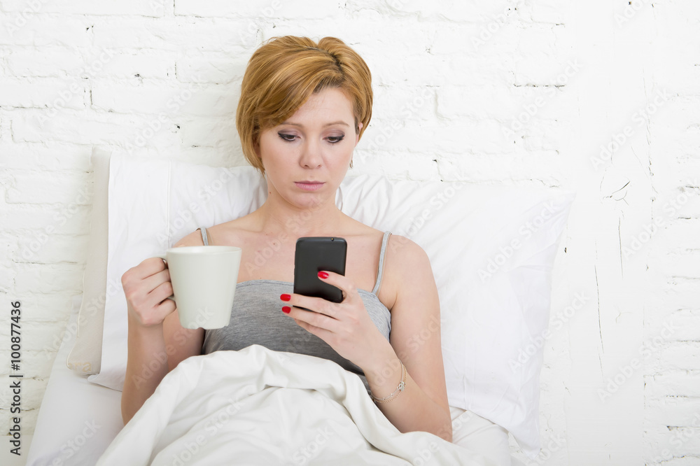 having coffe breakfast on bed while watching internet news in his mobile phone in online communication having coffe breakfast on bed while watching internet news in his mobile phone in online communication