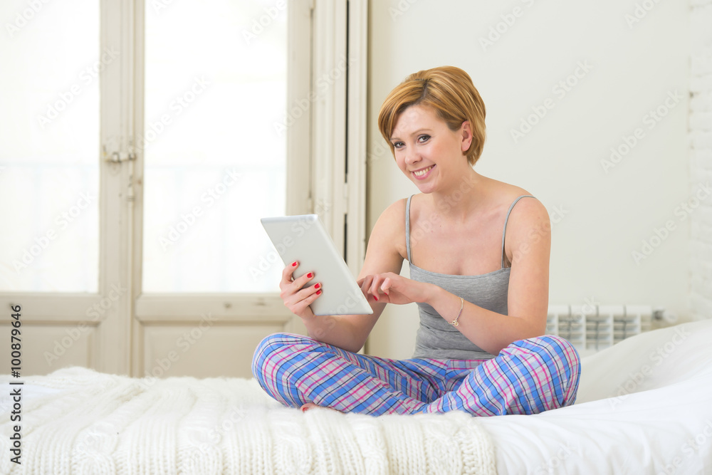 young attractive girl in sleeping pants sitting on bed using internet digital tablet pad young attractive girl in sleeping pants sitting on bed using internet digital tablet pad