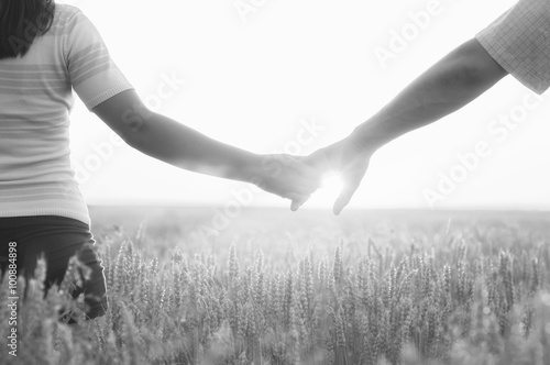 Young couple holding hands in the wheat field on sunny summer da