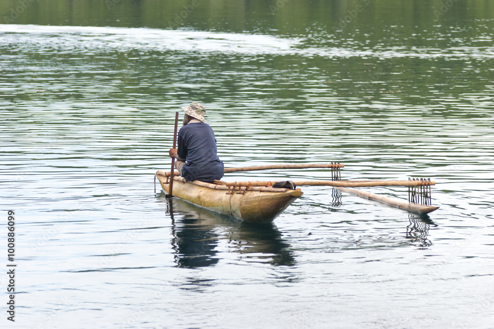 Fisherman in old wooden outrigger canoe in lagoon in Papua New Guinea Fisherman in old wooden outrigger canoe in lagoon in Papua New Guinea