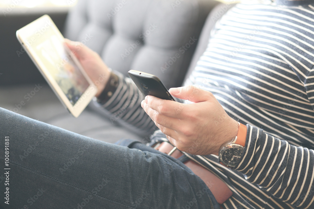 Young man sitting using a smart phone and holding a tablet , Dressed casually. Vintage post processed. Urban life style, technology, online, business, shopping, fashion and job hunting concept. Young man sitting using a smart phone and holding a tablet , Dressed casually. Vintage post processed. Urban life style, technology, online, business, shopping, fashion and job hunting concept.