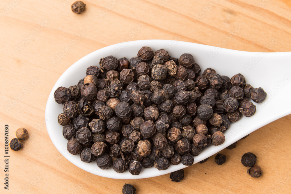 Spoonful of aromatic and spicy black pepper corns on wooden surface Spoonful of aromatic and spicy black pepper corns on wooden surface