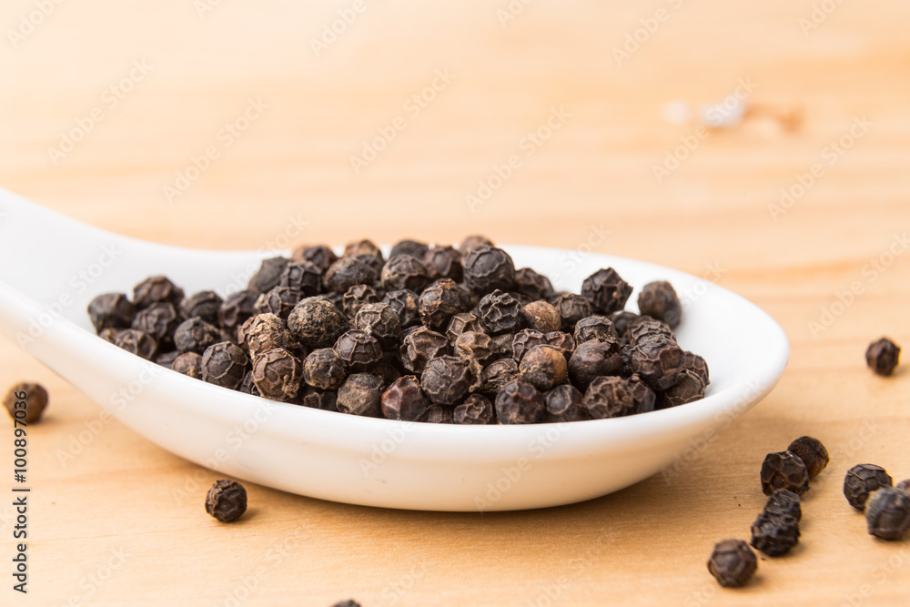 Spoonful of aromatic and spicy black pepper corns on wooden surface Spoonful of aromatic and spicy black pepper corns on wooden surface