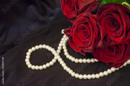 Beautiful red roses and pearls on black background