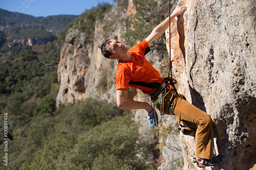 Young male climber hanging by a cliff.