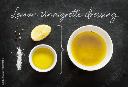 Lemon vinaigrette dressing - recipe ingredients on black chalkboard background from above. Lemon, olive oil, salt and pepper. Kitchen poster layout. photo