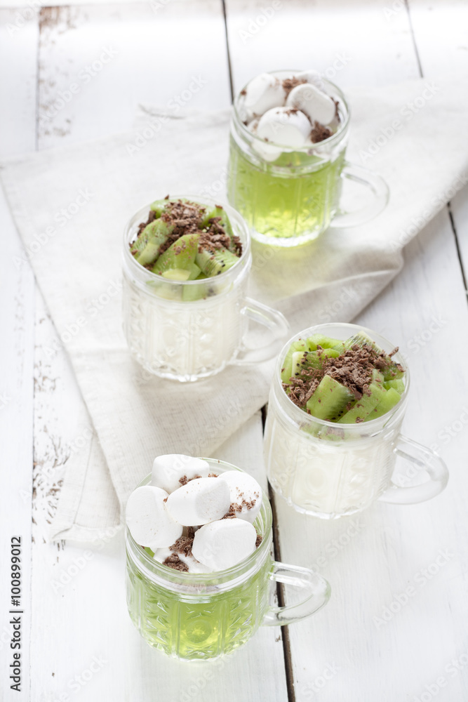 Jelly with kiwi fruit with marshmallows and grated chocolate in glass, sliced kiwi on white wooden table Jelly with kiwi fruit with marshmallows and grated chocolate in glass, sliced kiwi on white wooden table