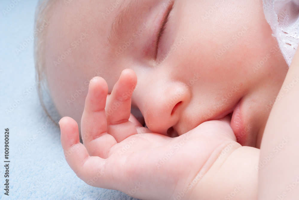 Baby sleeps with the finger in the mouth on a soft blue blanket, close up portrait