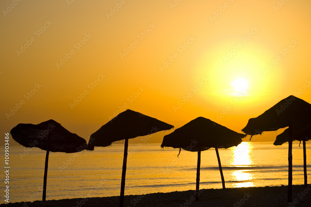 Silhouettes of parasols at the beach on sunrise/sunset background