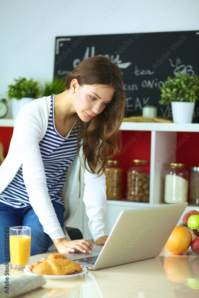 Attractive young woman using laptop and sitting in the kitchen Attractive young woman using laptop and sitting in the kitchen