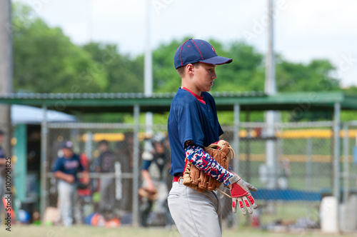 Youth baseball player walking off the field during game.