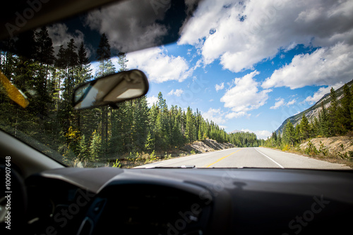 deserted road of the rocky mountains of alberta in the middle of peaks and forest seen from inside the car during a sunny day of summer
