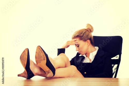 Tired young businesswoman holding legs on the desk
