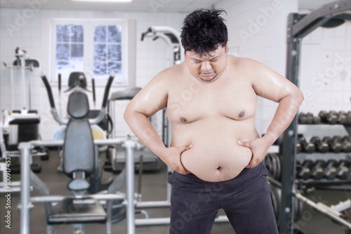 Overweight guy holds his stomach at gym
