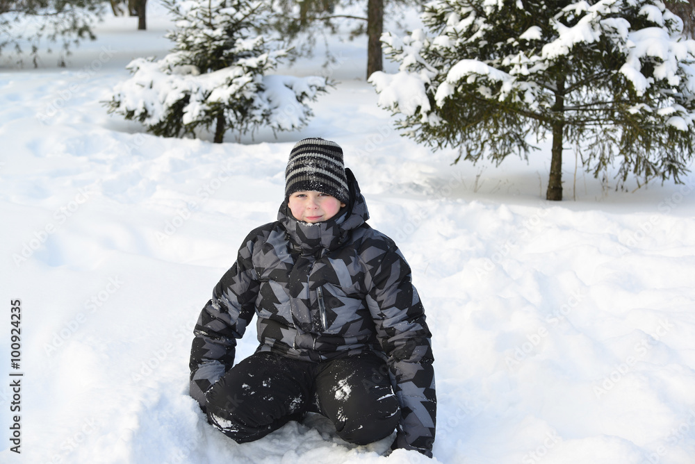 Teen boy sitting on   snow in the winter forest