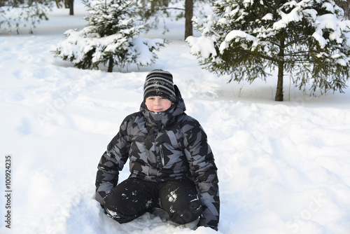 Teen boy sitting on snow in the winter forest