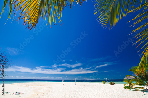 Tropical paradise: beautiful view through green palm foliage on a white sand beach in Maldives