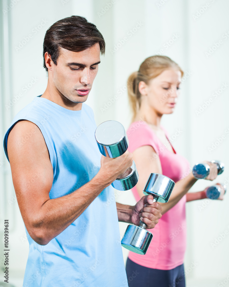 Couple exercising in gym, using weights Couple exercising in gym, using weights