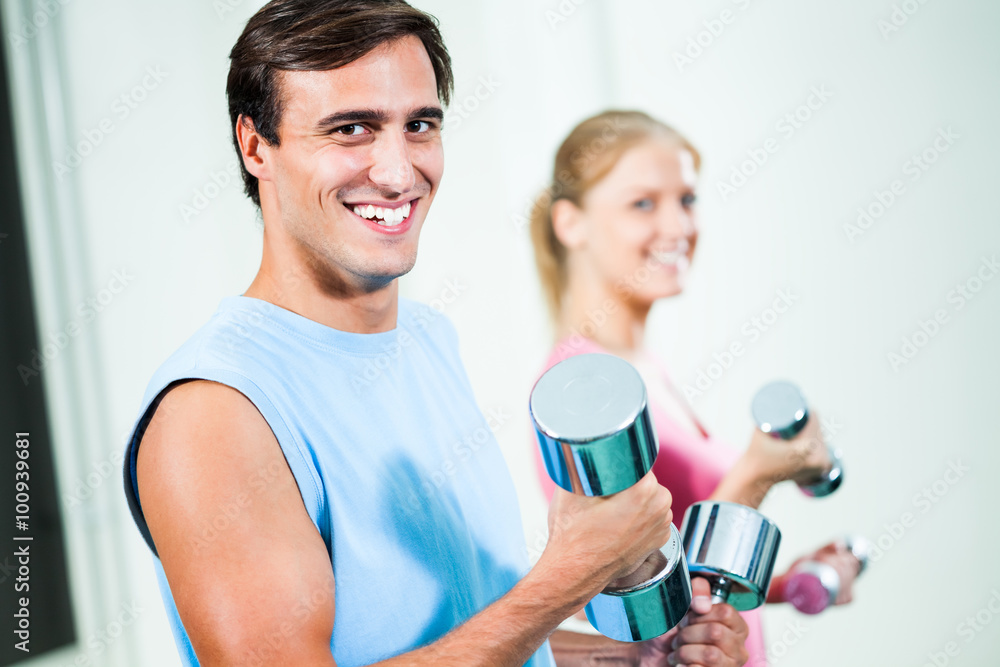 Couple exercising in gym, using weights Couple exercising in gym, using weights
