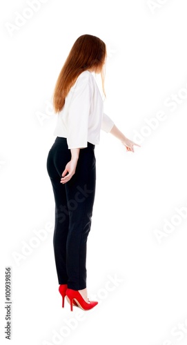 Back view of young redhead business woman pointing at wall.