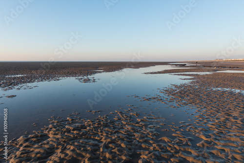 Beautiful sunny winters day on a british beach, with sand ripples and the sky reflecting in a water pool.