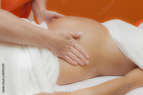 Pregnant young latina woman with beautiful skin  being wrapped with a towel  lying on a bed and having a relaxing prenatal massage  various techniques  glamour clarity effect