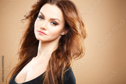 Close-up portrait of beautiful sexy young woman with long brown hair over brown background