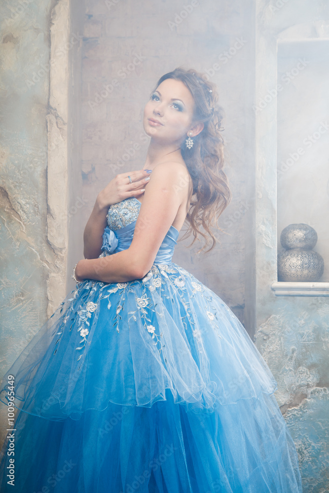 Beautiful young woman in gorgeous blue long dress like Cinderella with perfect make-up and hair style