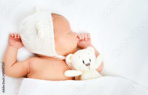 Cute newborn baby in bear hat sleeps with toy teddy bear