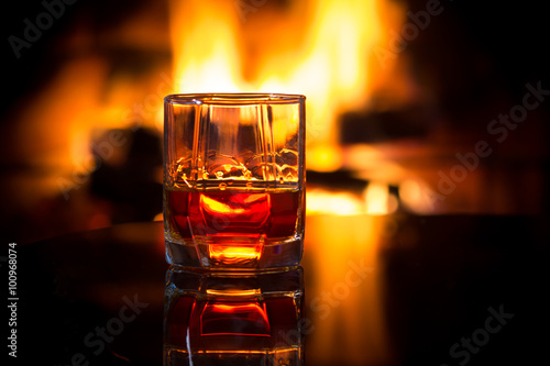 Glass of alcoholic drink in front of warm fireplace. Magical relaxed cozy atmosphere near  fire. Background horizontal