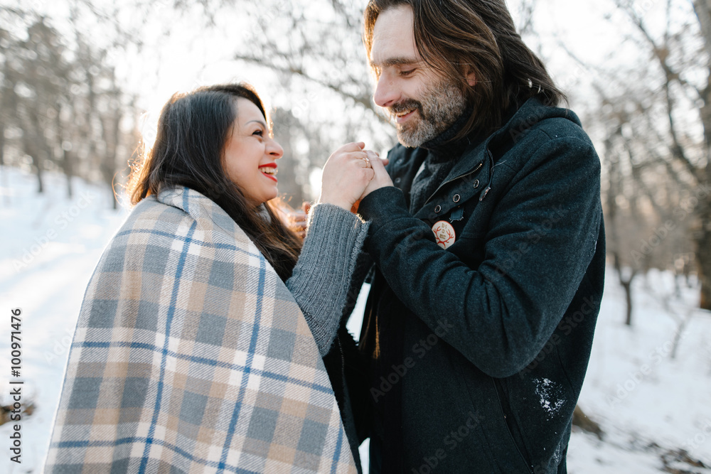 Fototapeta premium Cute young hipster man and pregnant mom having fun in winter park on a sunset hugging each other and smiling 