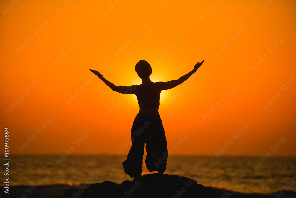 Female meditates during yoga and opens her body to the sun at a sunset