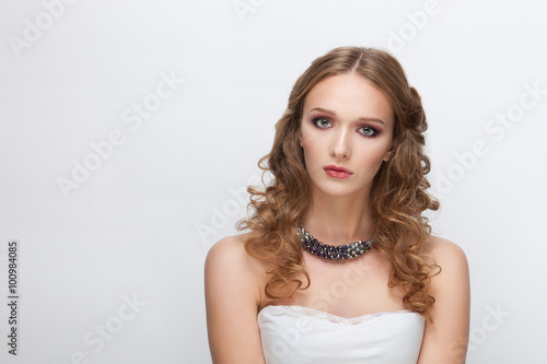 Young serious adorable blonde woman with curly hairstyle posing against white background