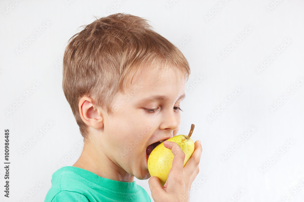 Little funny boy in a green shirt eating a yellow pear Little funny boy in a green shirt eating a yellow pear